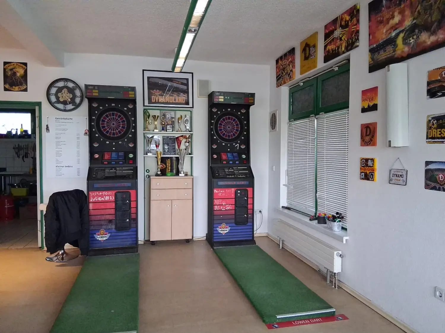Dartecke mit zwei Dartautomaten, grünen Wurfmatten und dem Pokalregal dazwischen