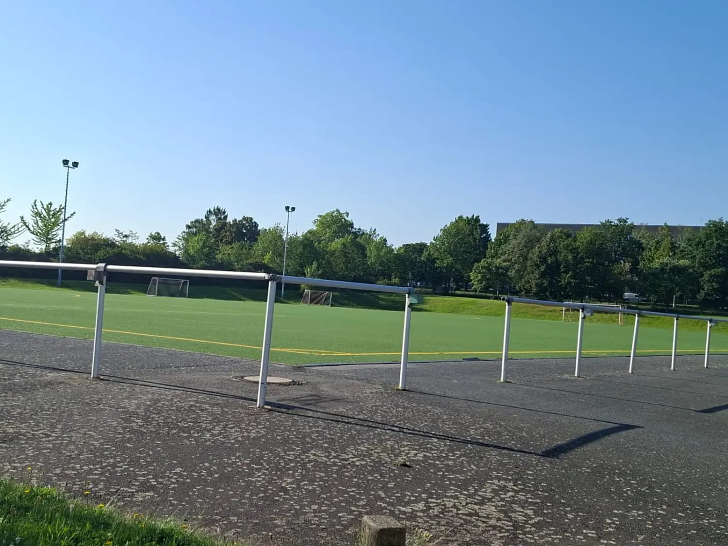 Sportplatz neben der Gaststätte in der Abendsonne, Bandenzaun im Vordergrund