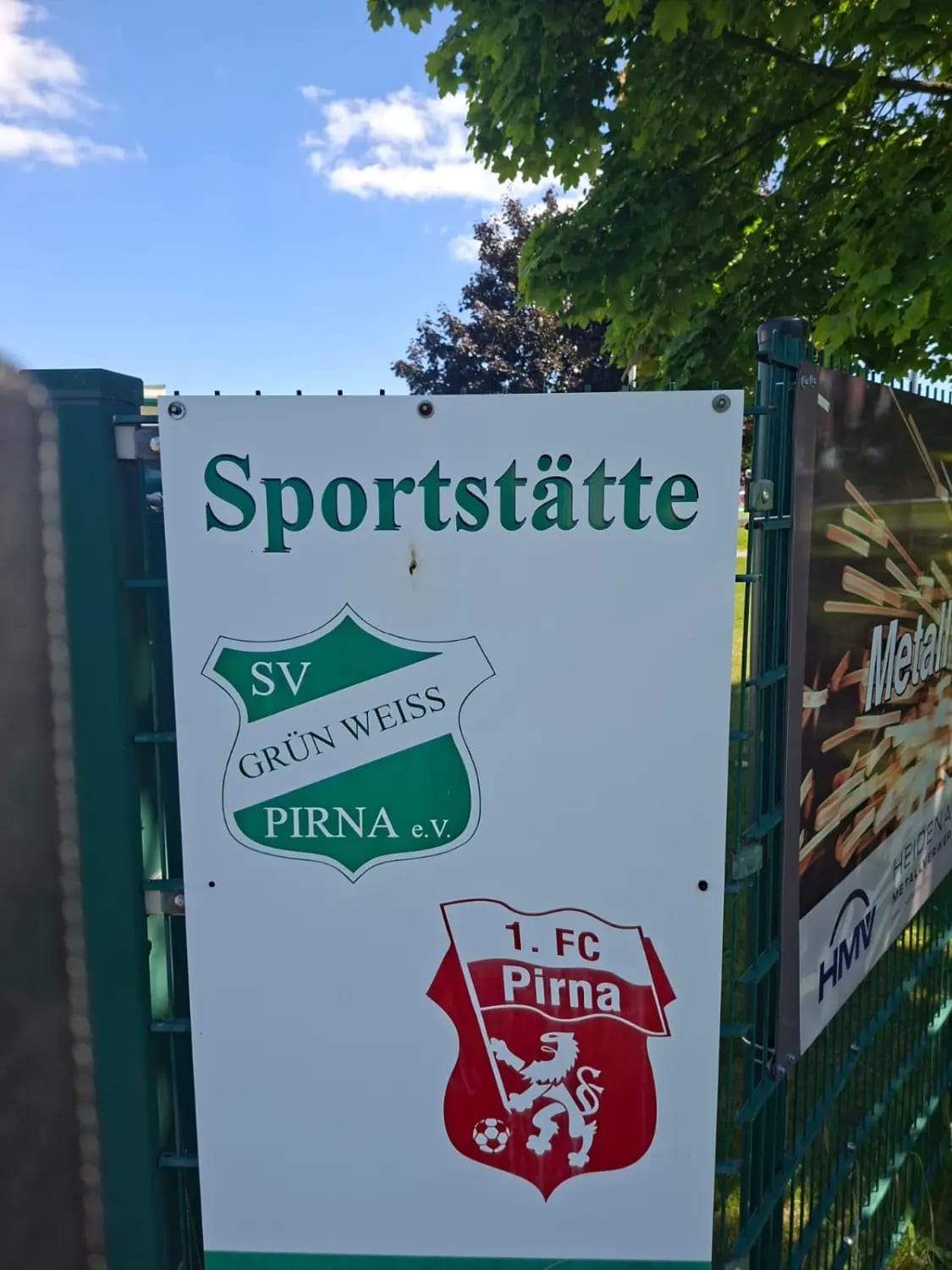 Schild „Sportstätte“ am Zaun mit den Wappen von SV Grün-Weiß Pirna e.V. und 1. FC Pirna e.V.